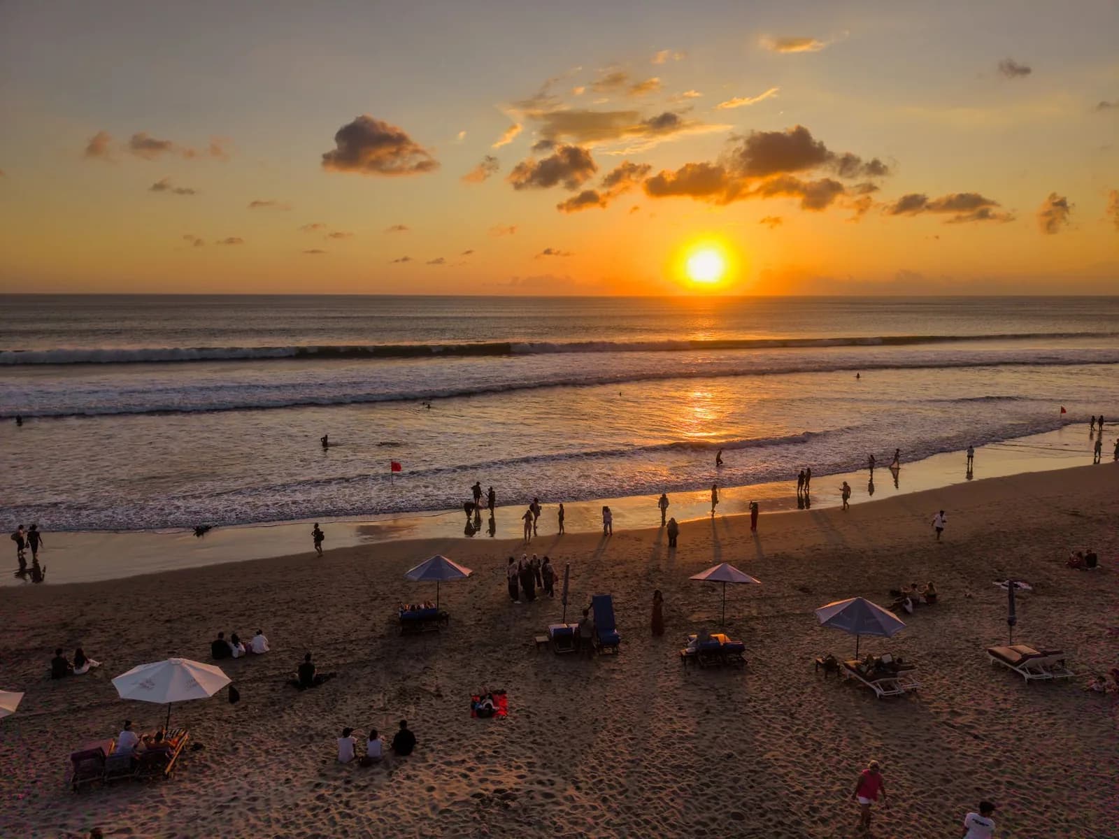 Sunset over Kuta Beach in Bali, with visitors on the wide sand beach and waves rolling in