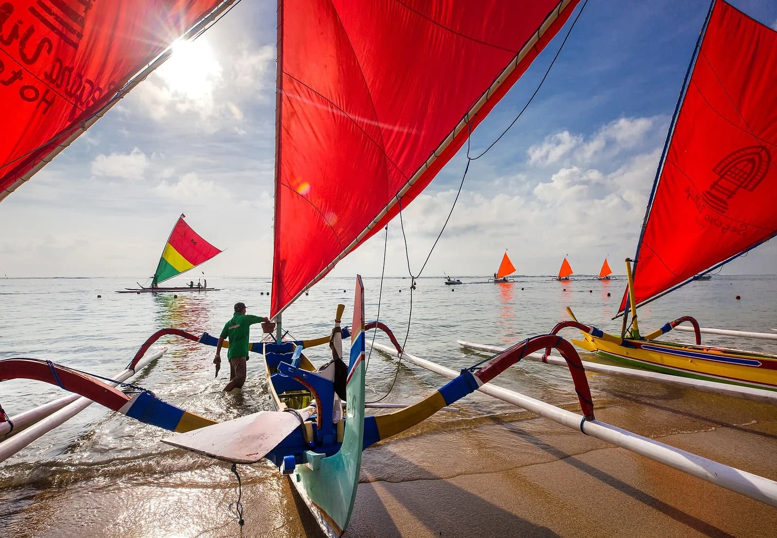 Brightly painted jukung outrigger boats with red sails on the calm lagoon at Sanur Beach, Bali